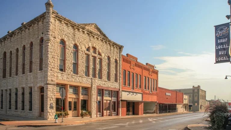 A two-story limestone commercial building and red brick storefronts on a corner in downtown Stephenville