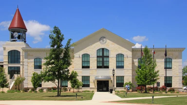 Kerrville City Hall, a cream stone building with a red-roofed clock tower, under a blue sky