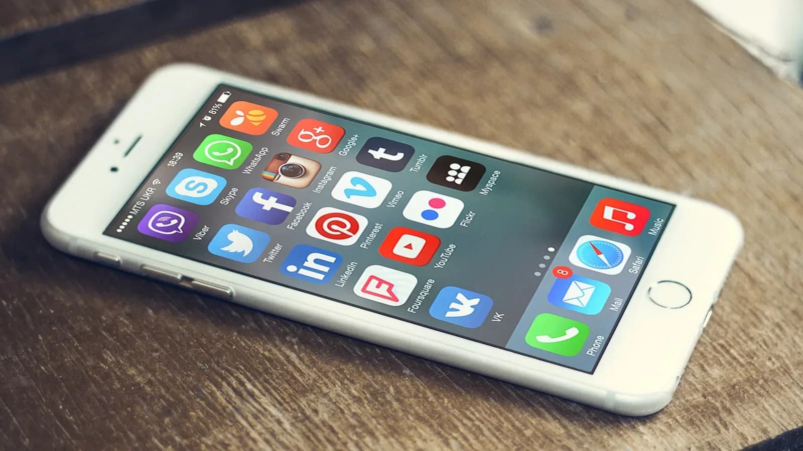 A white smartphone lying on a wooden table with social media app icons on its screen