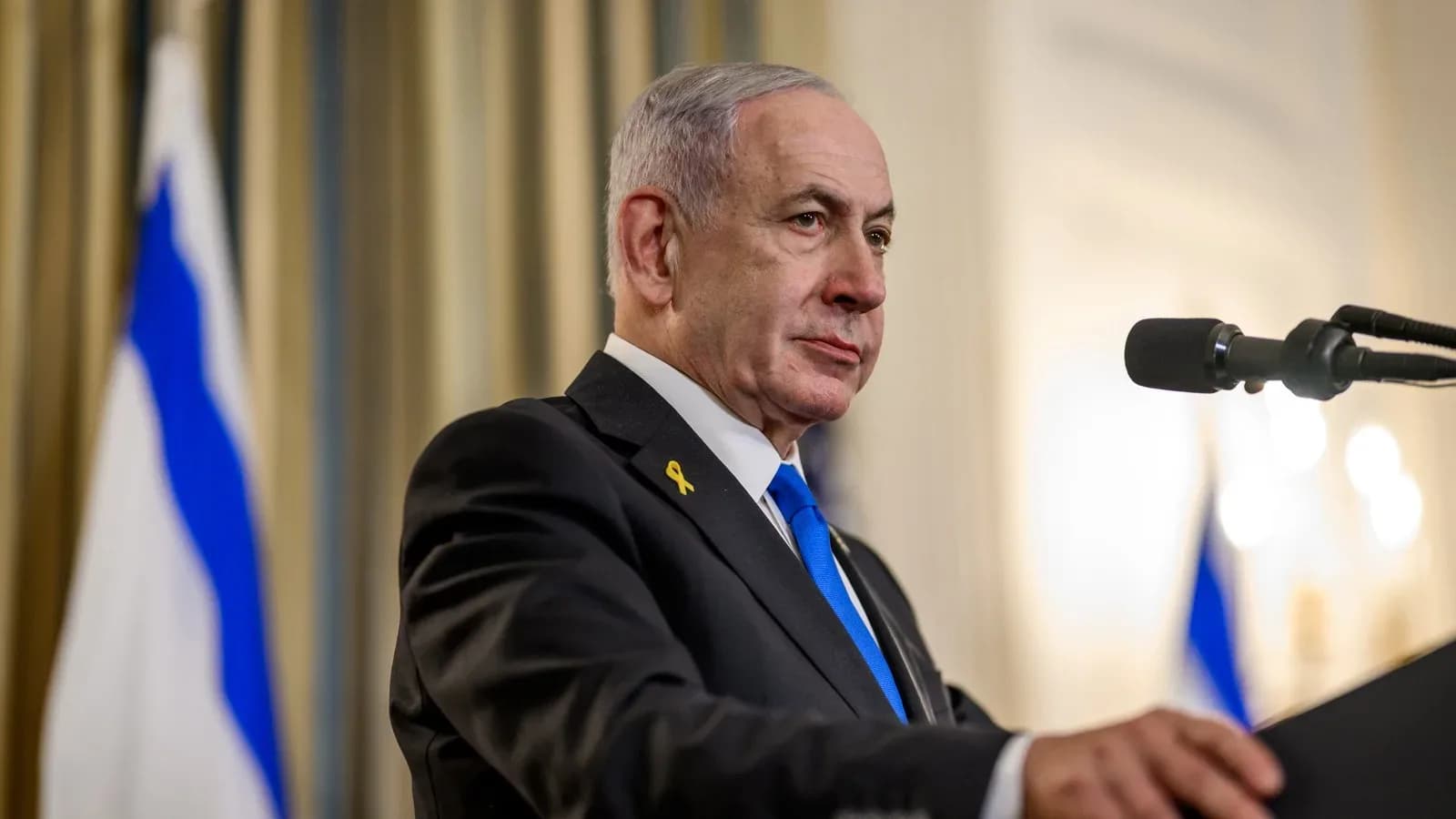 Israeli Prime Minister Benjamin Netanyahu speaking at a microphone with an Israeli flag behind him