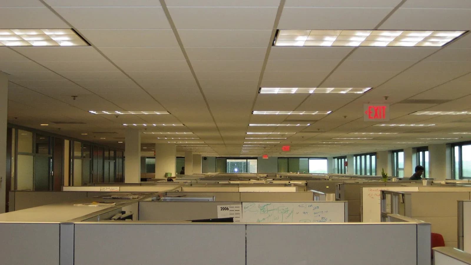 Rows of empty beige office cubicles stretching toward windows under fluorescent ceiling lights