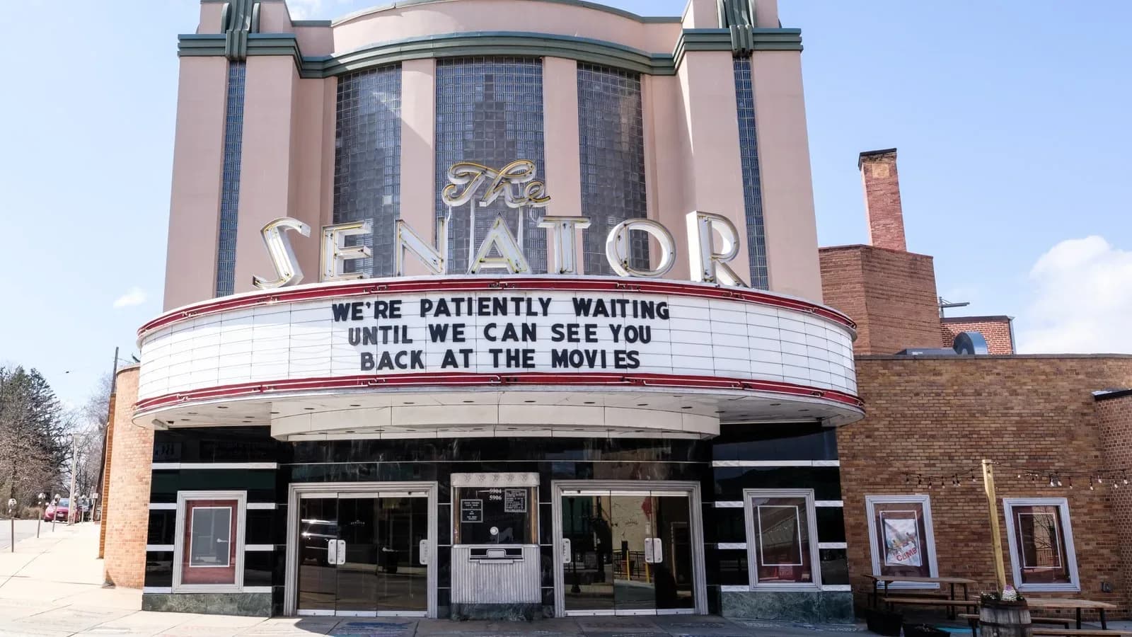The Art Deco Senator Theatre in Baltimore with its marquee reading We are patiently waiting until we can see you back at the movies