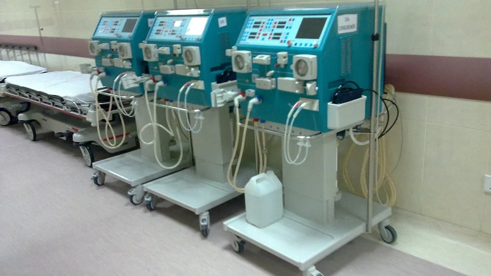 A row of dialysis machines beside hospital beds in a treatment room