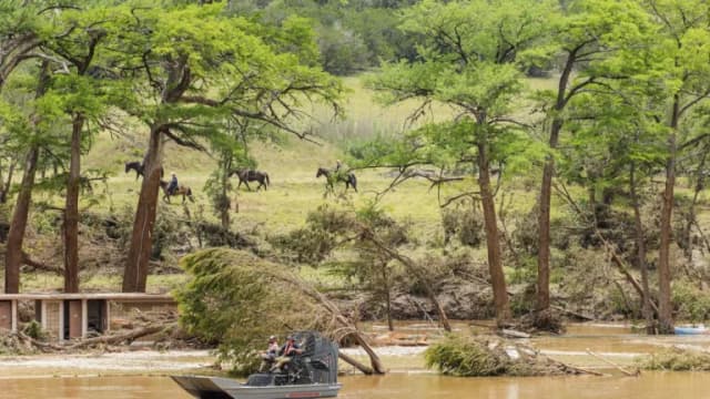 An airboat and riders on horseback along a flood-damaged riverbank in Kerrville