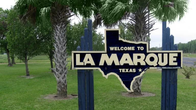 A Texas-shaped Welcome to La Marque sign between two palm trees