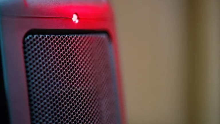 Close-up of the front grille of an electric ceramic space heater with a glowing red indicator light