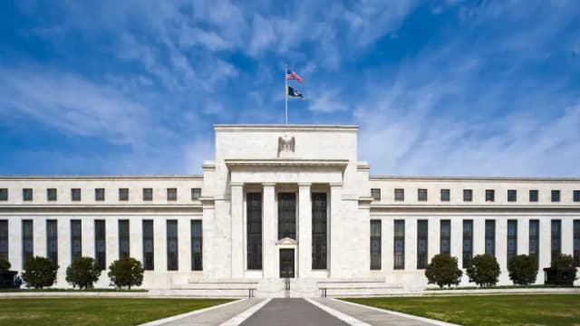 The white marble Eccles Building, headquarters of the Federal Reserve, under a blue sky with an American flag on top