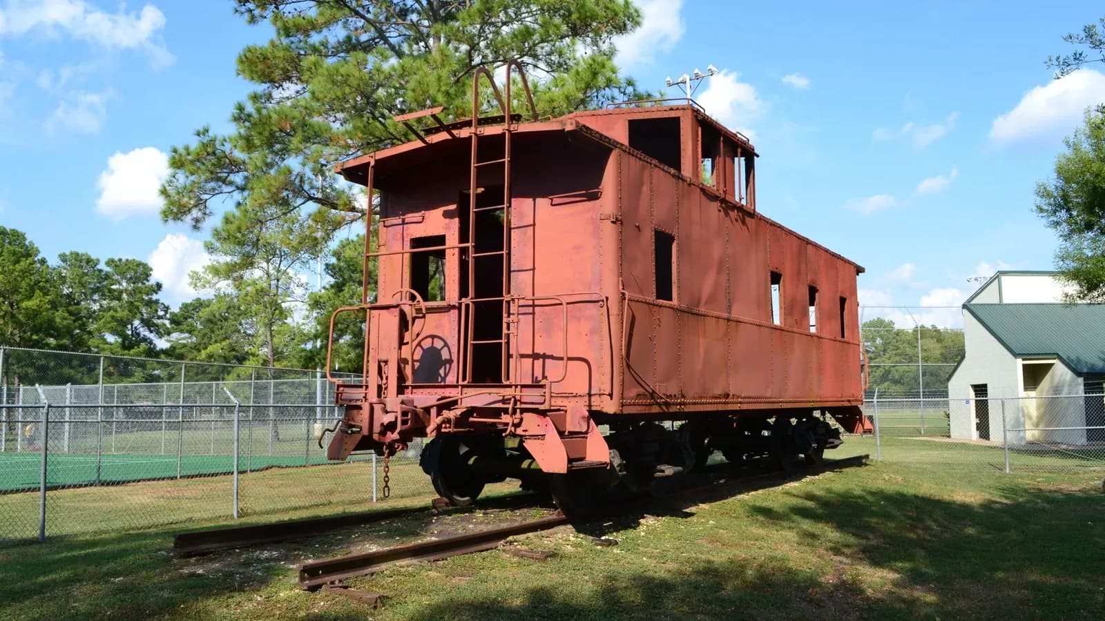 A red Southern Pacific caboose on display under trees at Crosby Park in Crosby, Texas