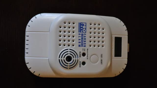 A white plug-in carbon monoxide alarm with a test button and digital display on a dark background