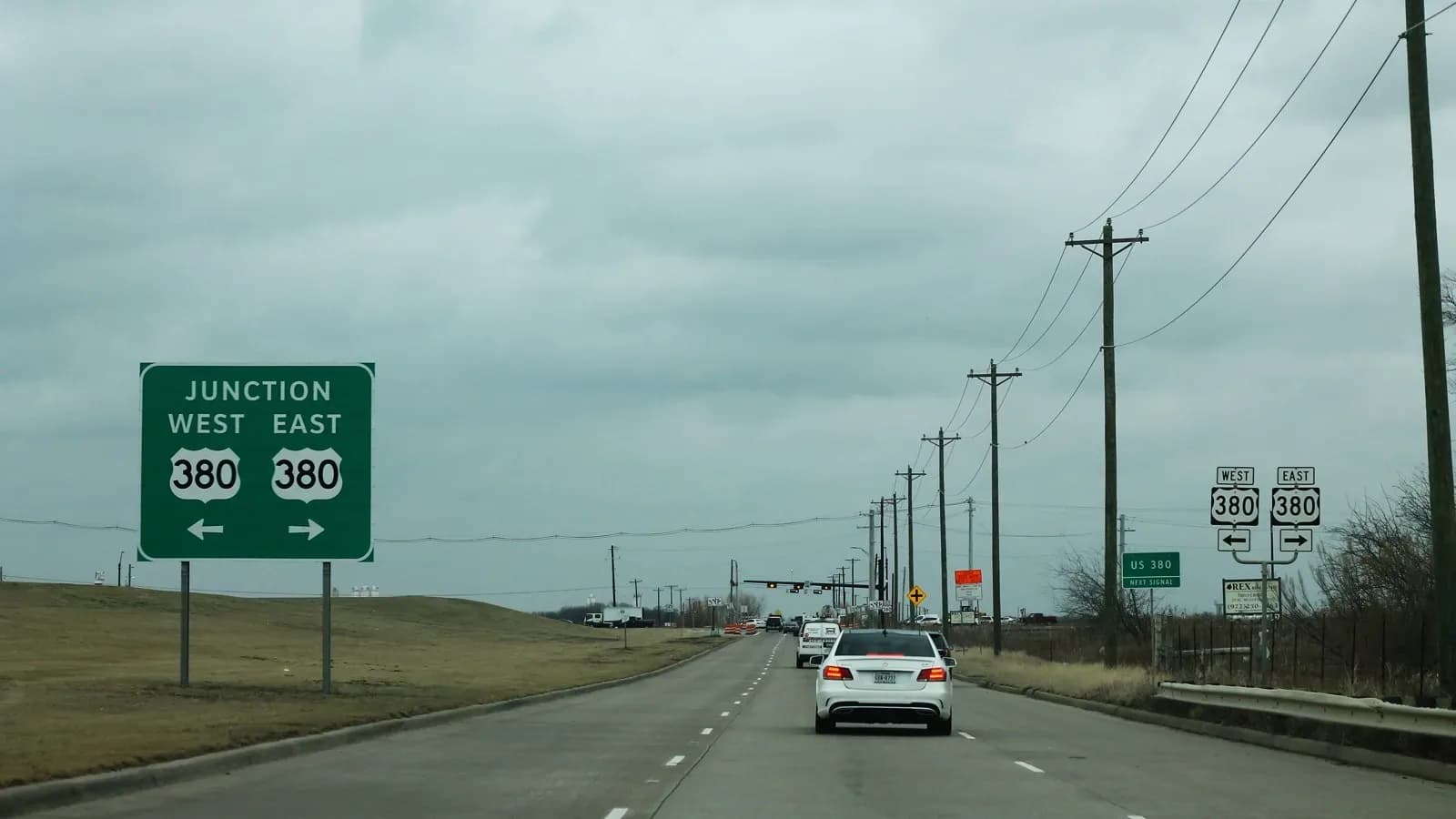 A four-lane road with a green Junction West East 380 sign and traffic heading toward U.S. 380 under a cloudy sky
