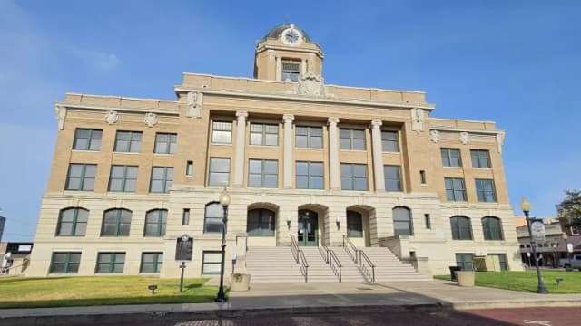 The tan stone Cooke County Courthouse in Gainesville with columns, a clock dome and a wide front staircase under a blue sky