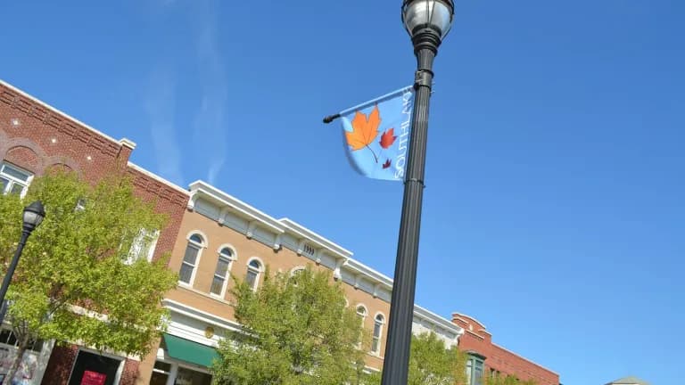 Red brick storefronts at Southlake Town Square with a lamppost and a hanging banner under a bright blue sky
