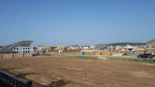 New houses and empty graded lots in a growing Austin subdivision under a clear sky