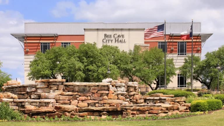 Bee Cave City Hall with American and Texas flags, trees and a stacked limestone wall in front