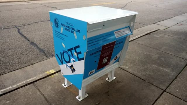 A blue and white official absentee ballot drop box on a sidewalk in Madison, Wisconsin