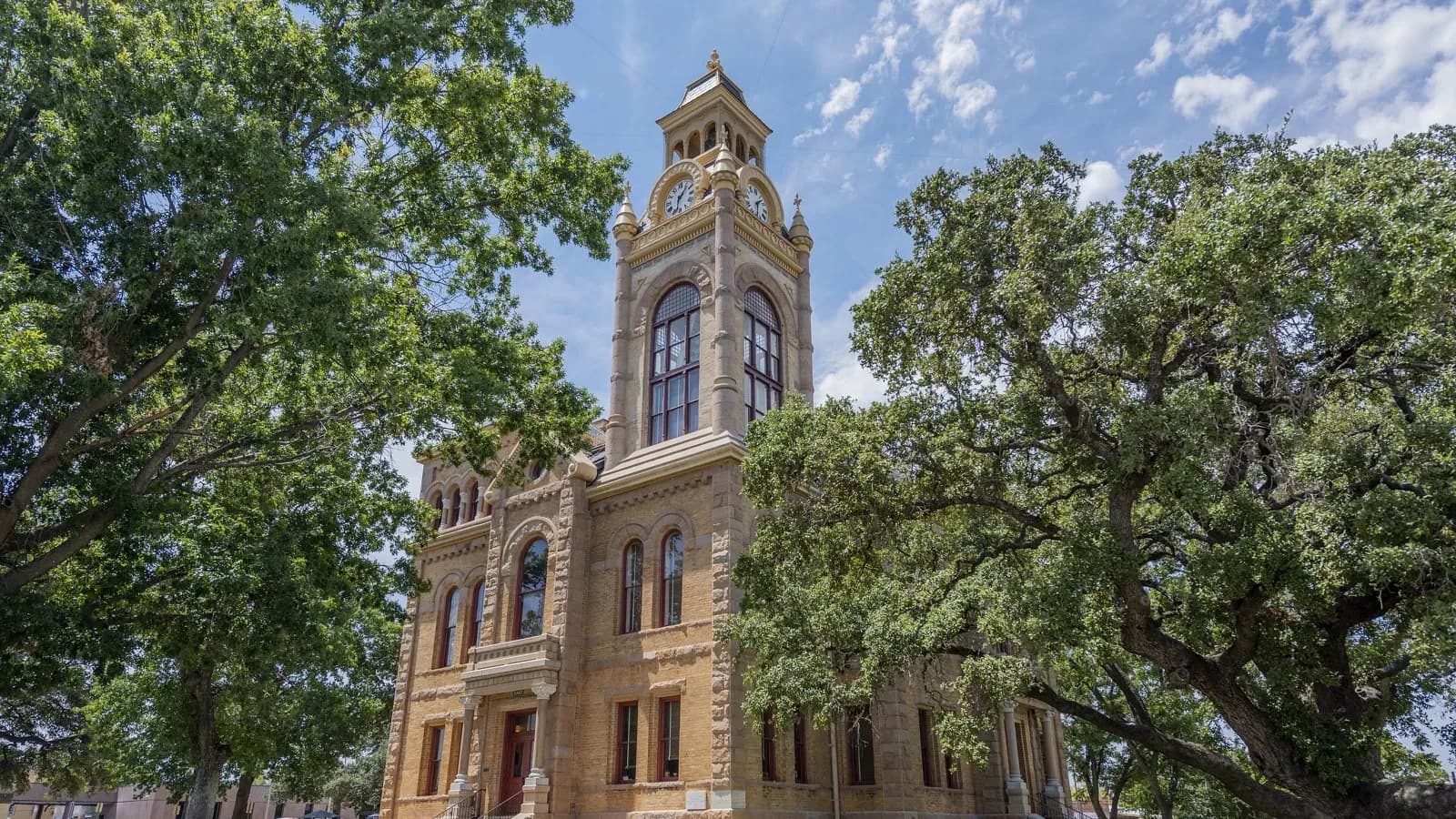 The sandstone Llano County Courthouse with its clock tower, framed by large oak trees