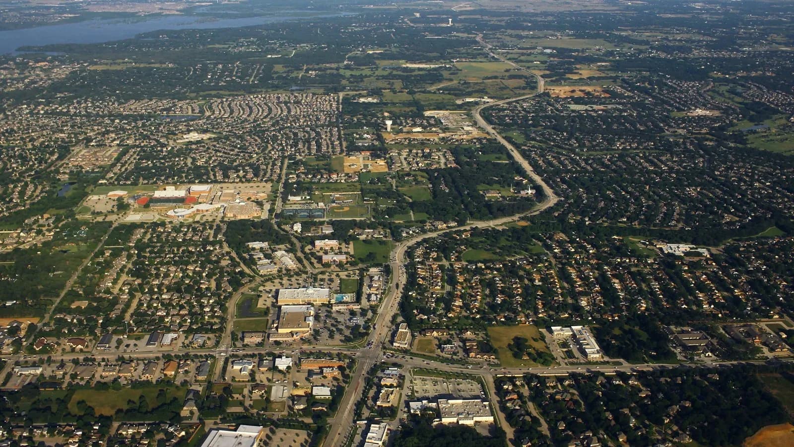 Aerial view of Flower Mound neighborhoods, shopping centers and a winding road, with a lake in the distance