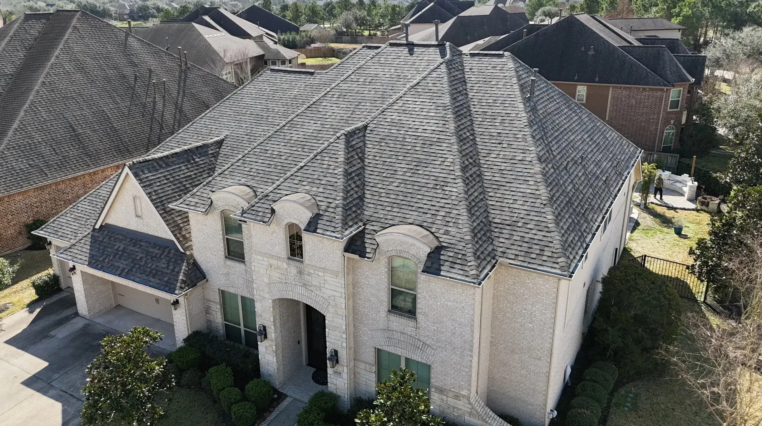 A light stone house in a Houston-area subdivision with a new gray architectural shingle roof.