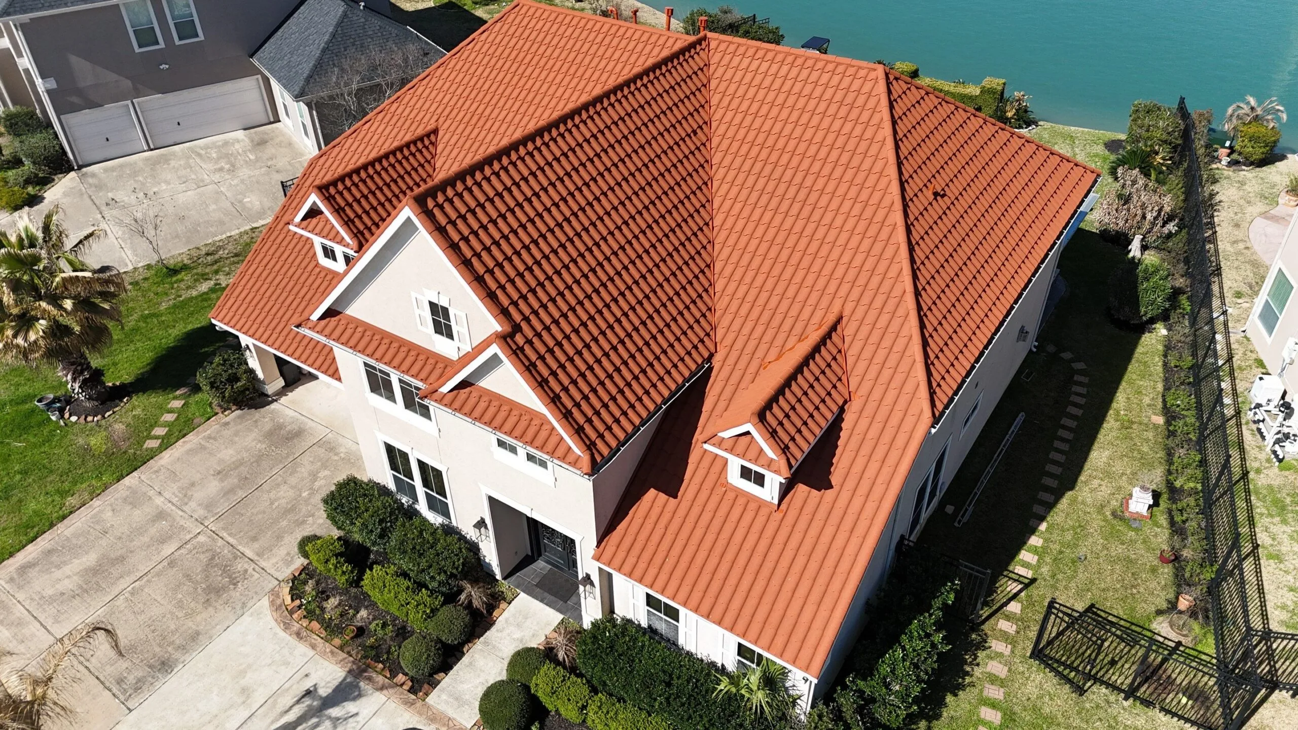 A red tile roof on a two-story house beside the water.