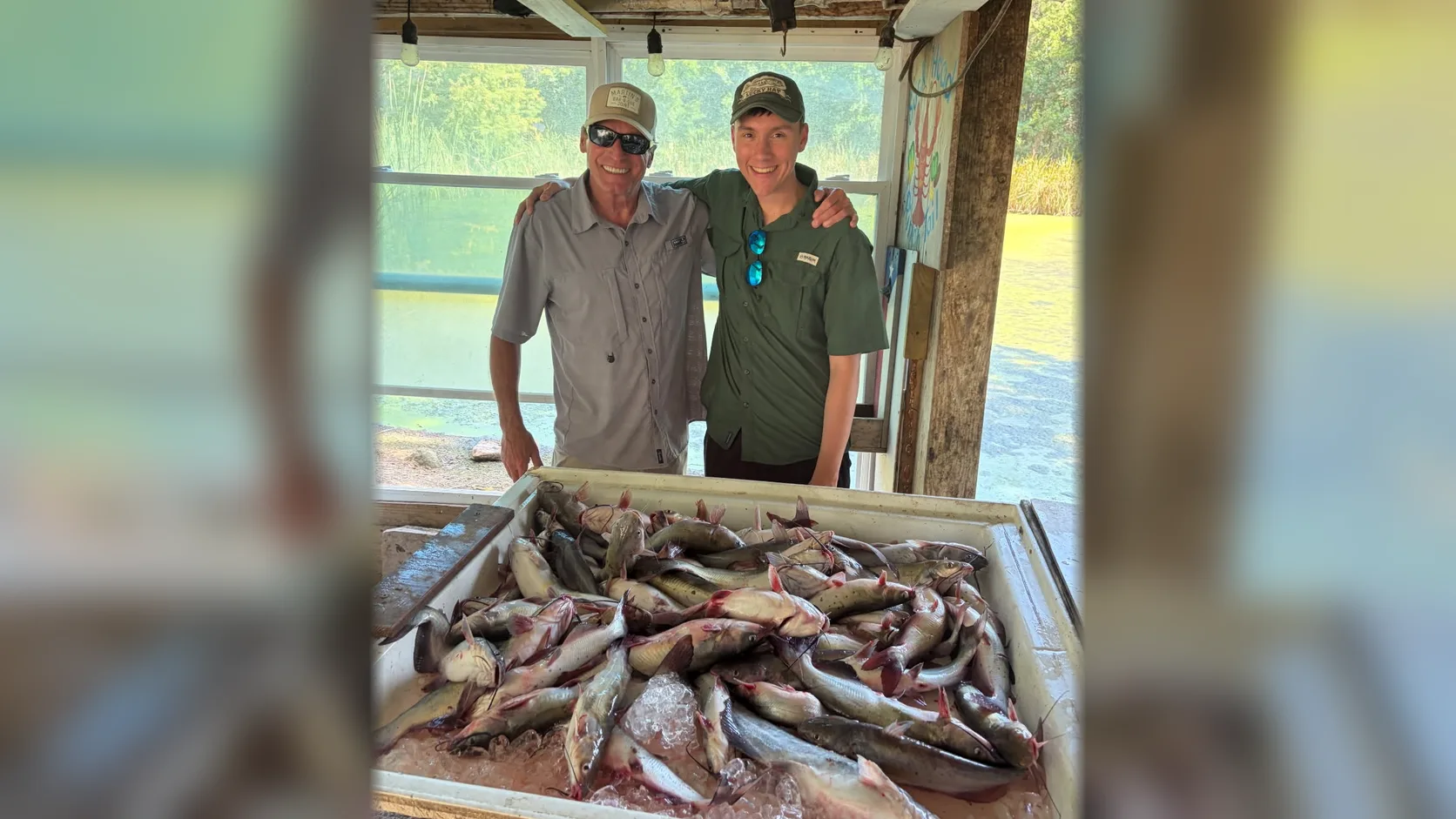 Phillip and Brandon stand behind a large catch of catfish on ice.