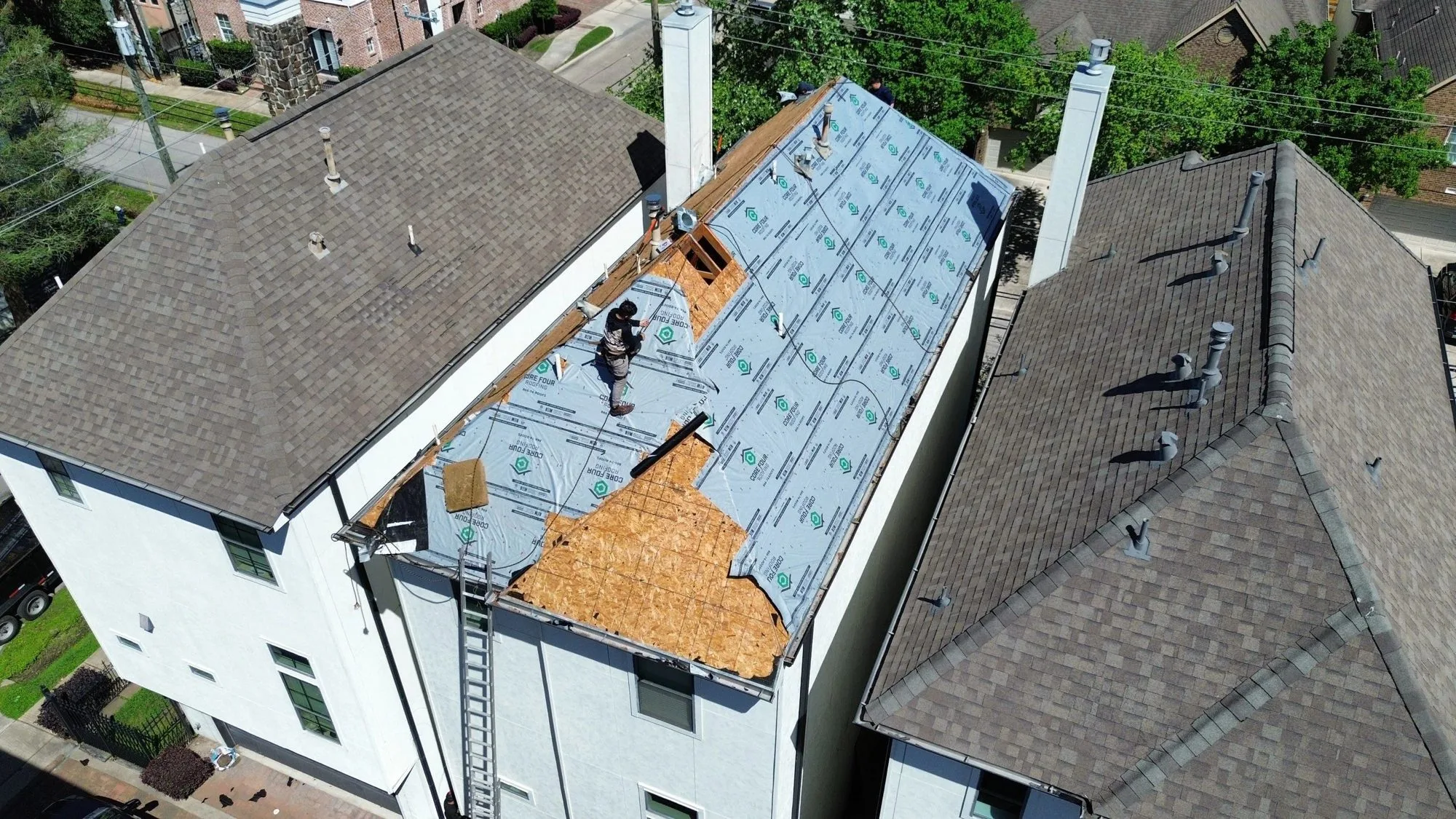 A residential roof replacement in progress, with synthetic underlayment on part of the deck and bare plywood still exposed