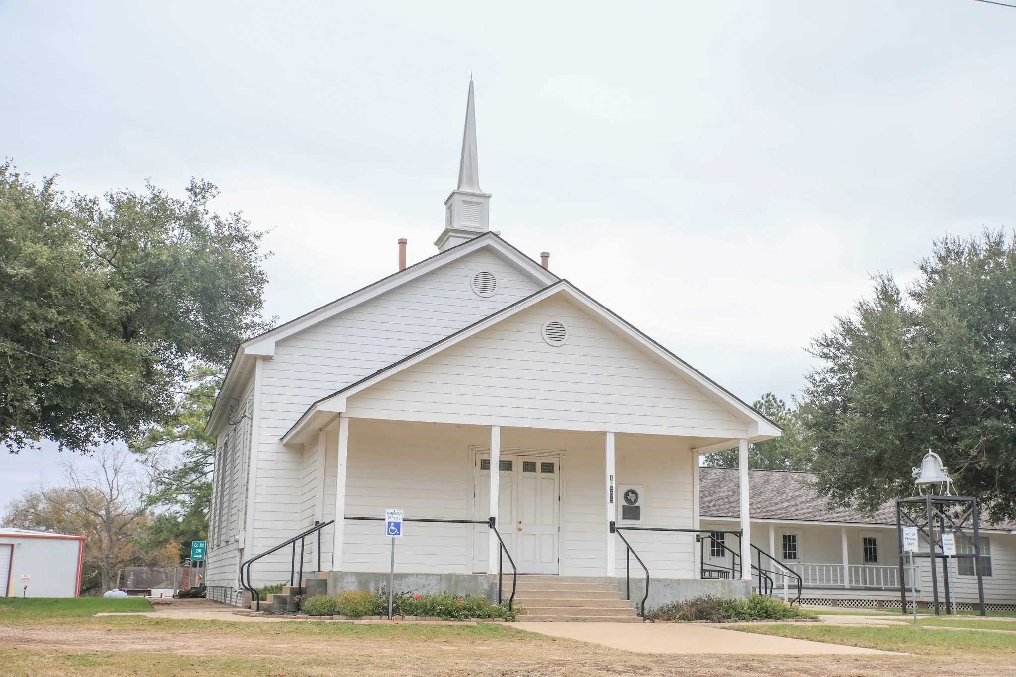 White wood-frame Plantersville Baptist Church with a steeple, a front porch, and a bell on the lawn