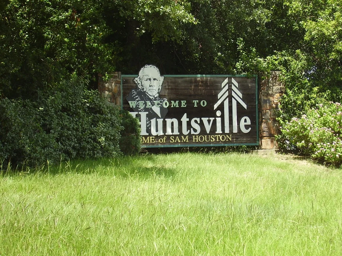 Welcome to Huntsville sign reading Home of Sam Houston, with trees behind it