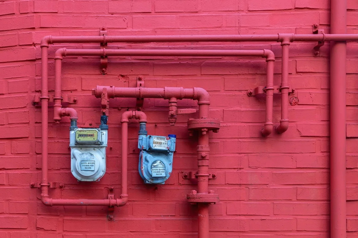 Two blue water meters mounted on a red brick wall with pipes