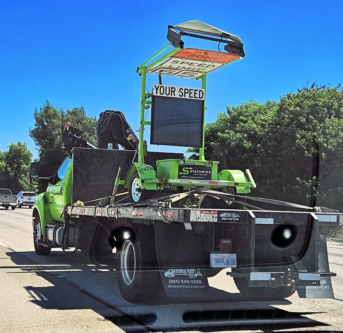 A portable radar speed display sign on a trailer being hauled on a flatbed truck