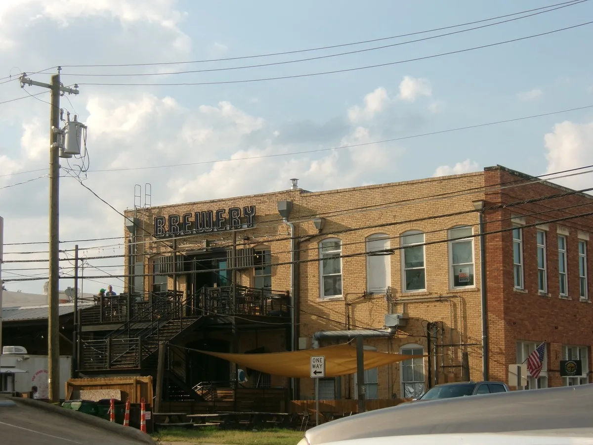 A two-story brick building with a brewery sign and an outdoor stairway beside power poles in Pflugerville