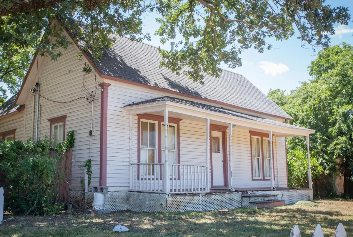 White wood-frame historic house with a front porch under large shade trees in Mansfield