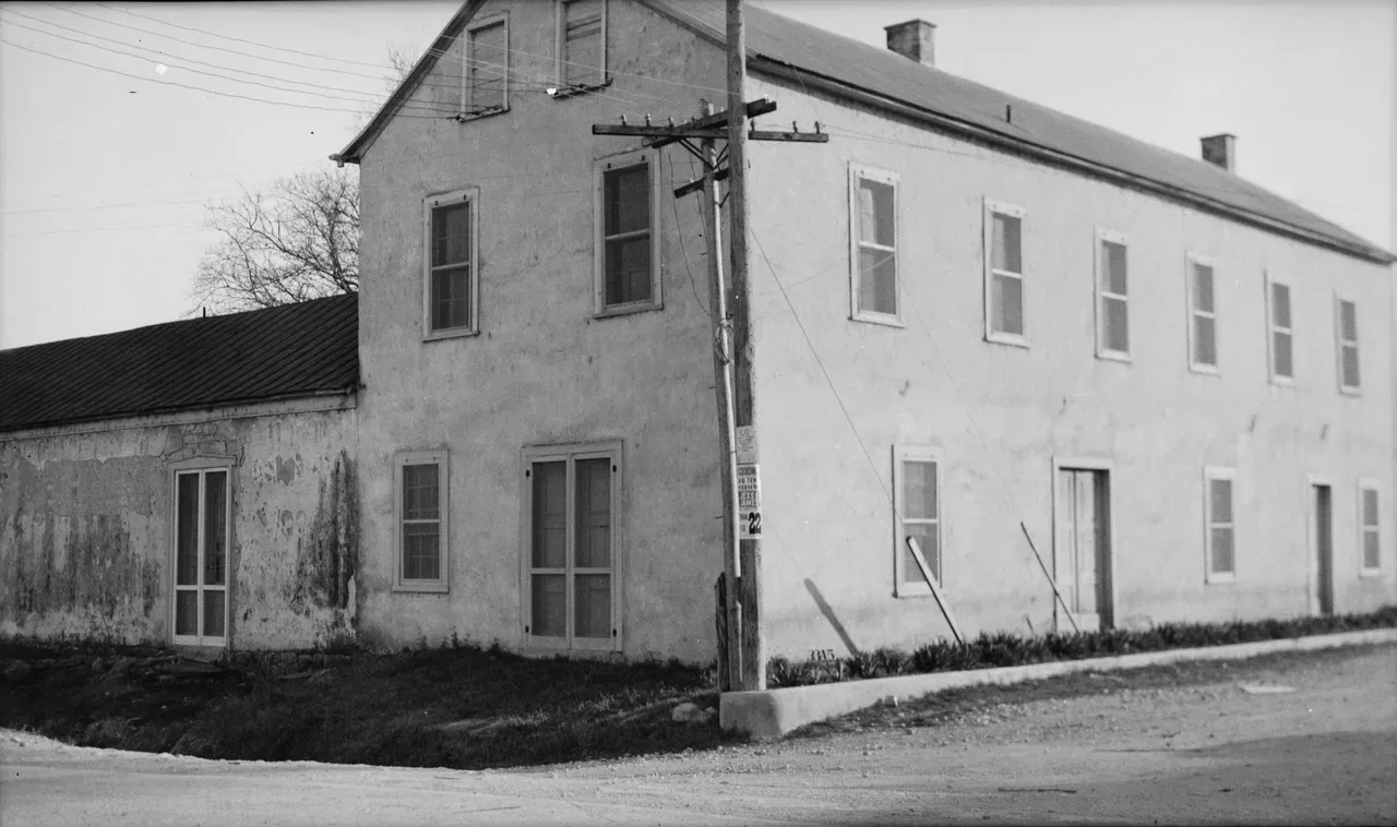 Black-and-white 1934 photograph of the two-story plastered stone Vance Hotel in Castroville, Texas, at a street corner, with a lower one-story wing at left and a utility pole in front