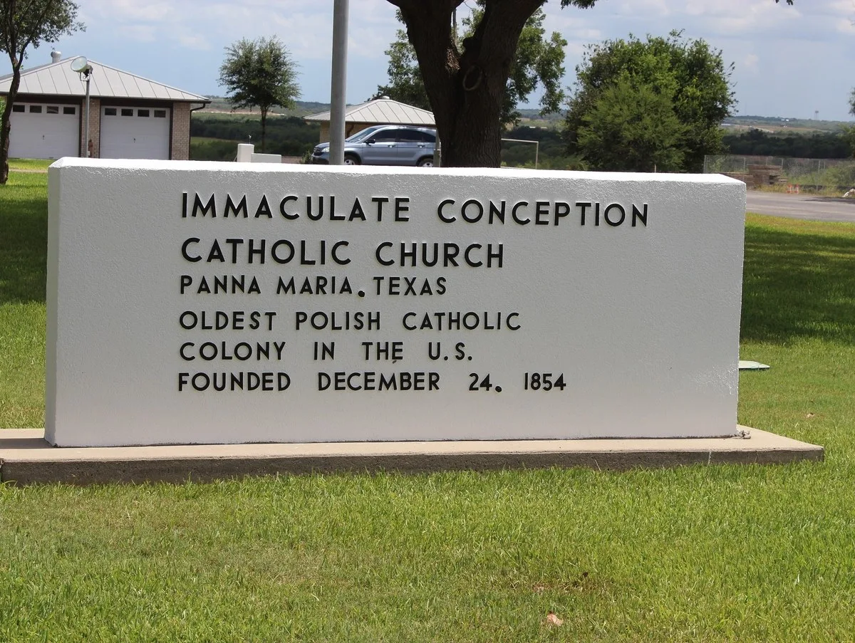 A white stone sign reading Immaculate Conception Catholic Church, Panna Maria, Texas, oldest Polish Catholic colony in the U.S., founded December 24, 1854