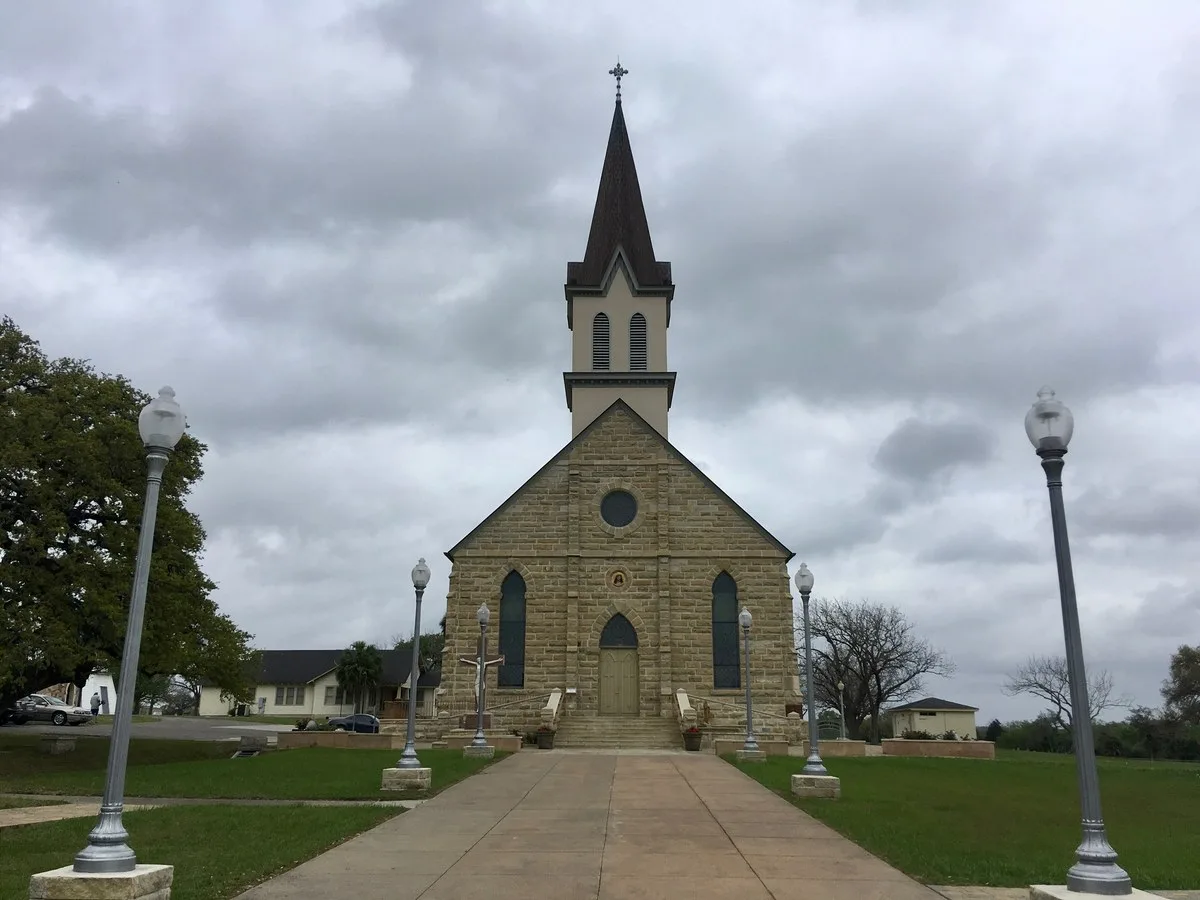 The stone south facade and tall spire of St. Mary's Church of the Assumption in Praha, Texas
