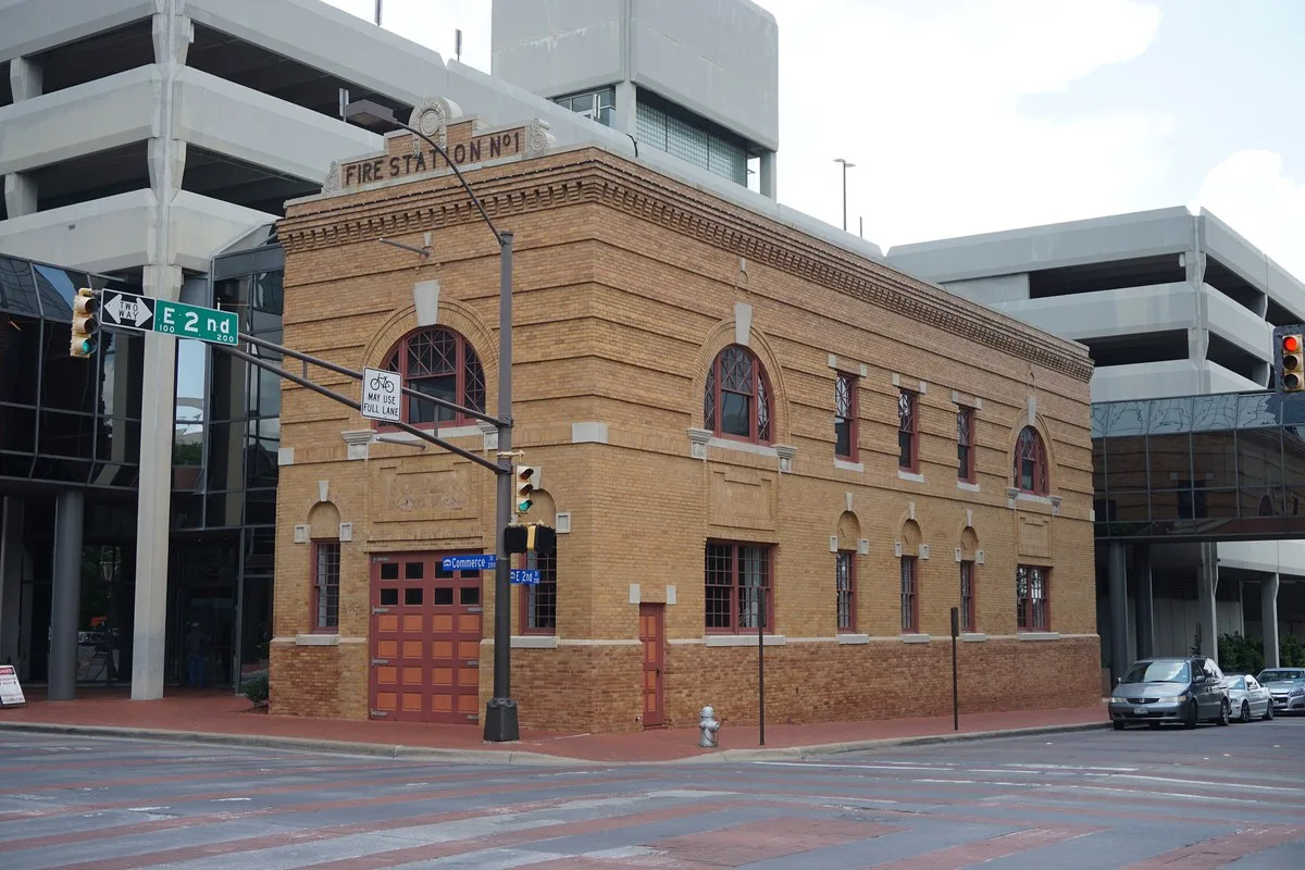 A red brick fire station with arched bay doors on a city street in Fort Worth
