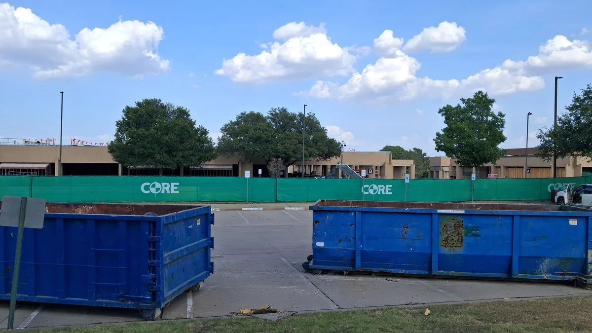Construction cranes and a partly built school building behind a fence on a summer day