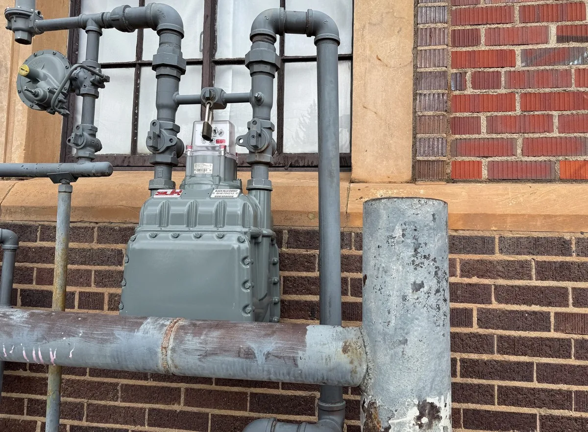 Close-up of a residential natural gas meter with dials and yellow piping beside a house