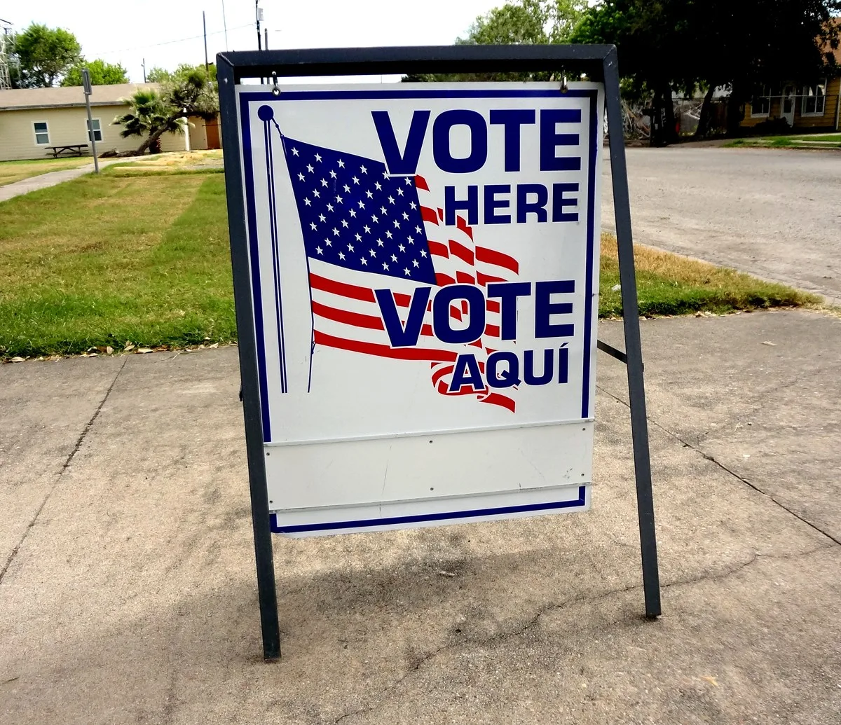 A white Vote Here sign with a red arrow posted outside a polling place in Texas
