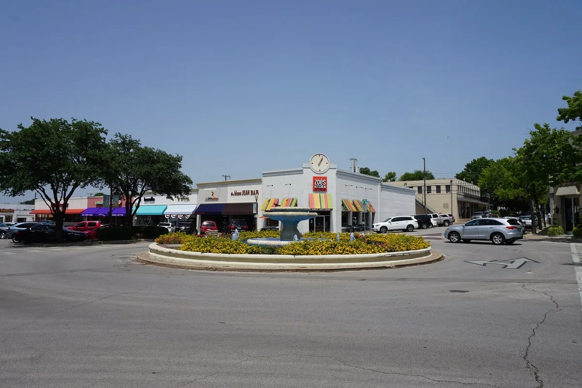 A round fountain and flower bed in front of shops and parked cars at Snider Plaza