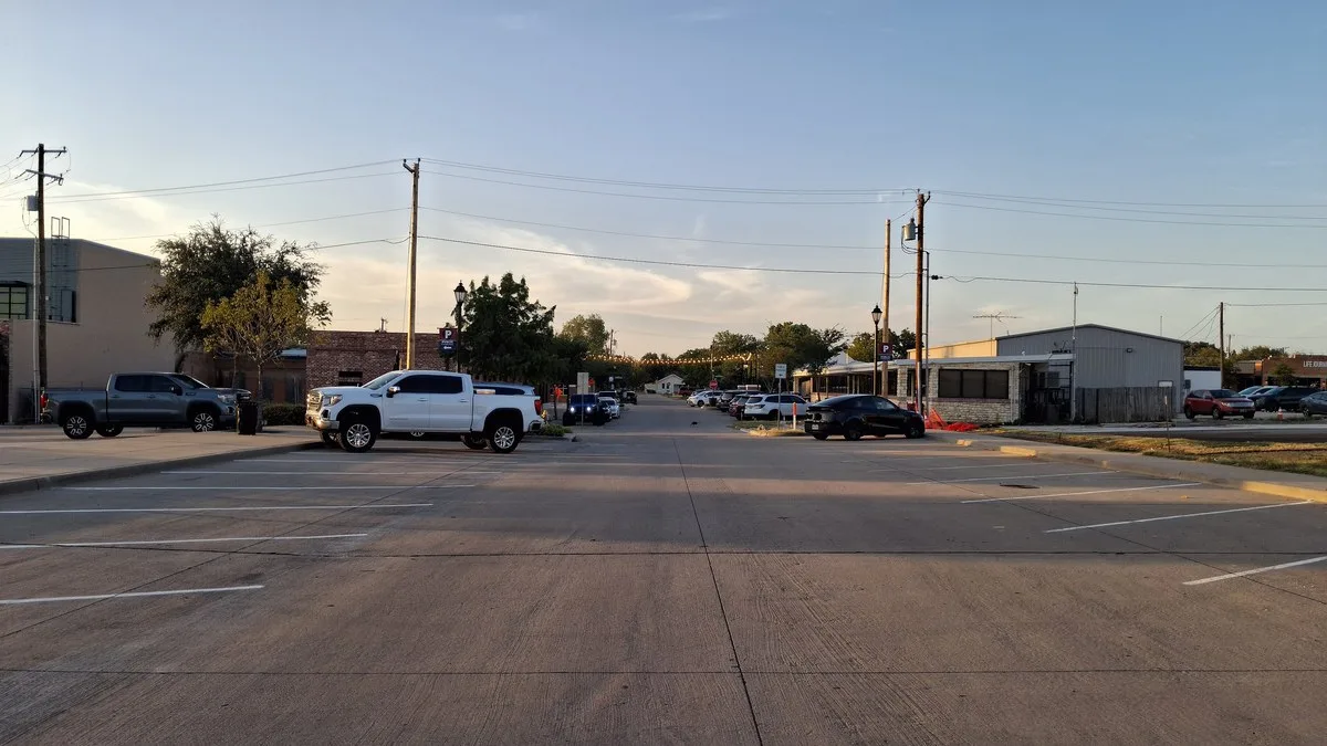 A wide, quiet Main Street in downtown Prosper with parked pickups and low commercial buildings at sunset