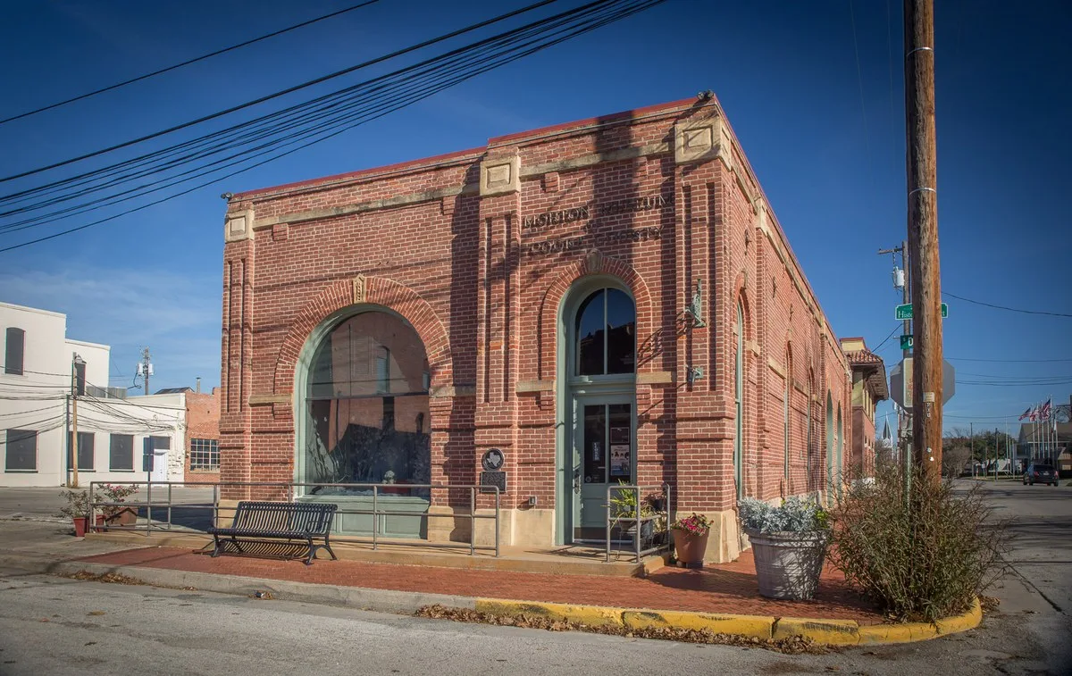 A red brick building with arched windows and Morton Museum of Cooke County lettering on a corner in downtown Gainesville