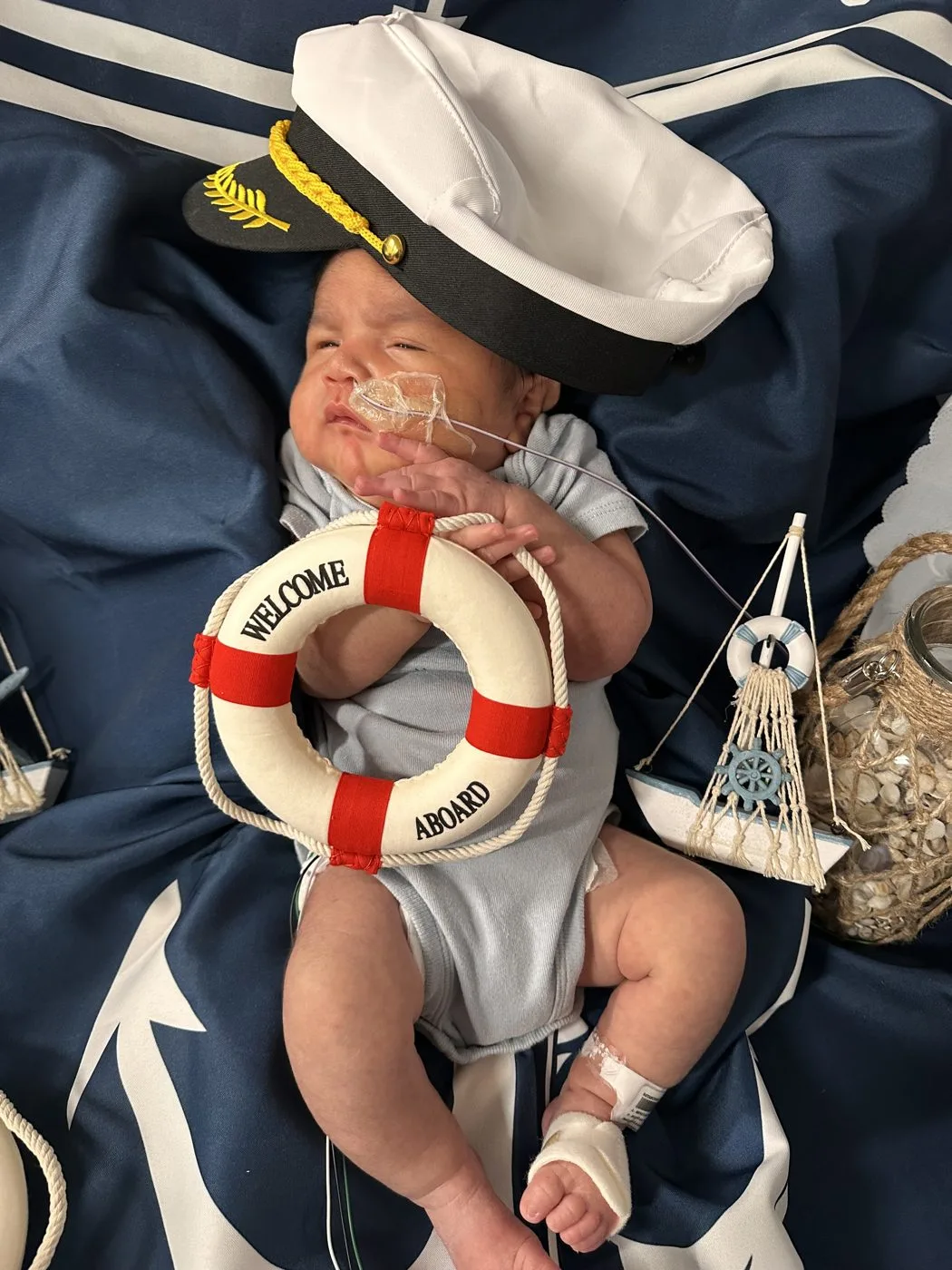A baby in the HCA Houston Healthcare Conroe NICU dressed as a sailor captain, wearing a captain hat and holding a Welcome Aboard life ring