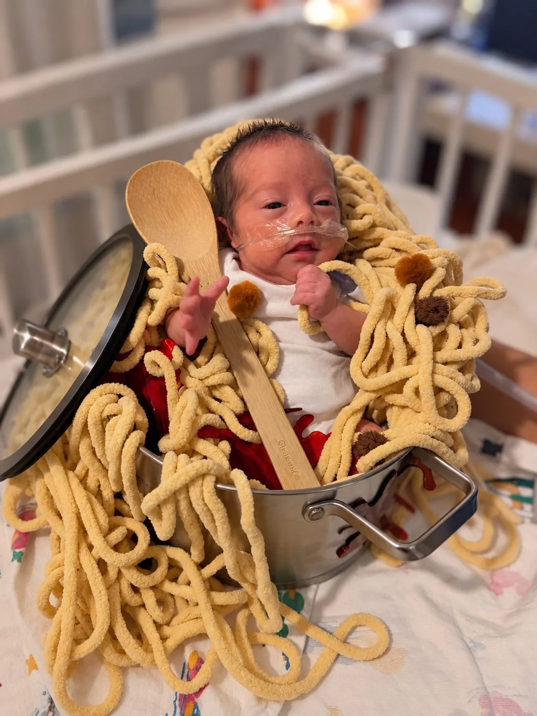 A baby in the HCA Houston Healthcare Conroe NICU dressed as spaghetti and meatballs, sitting in a cooking pot with yarn noodles and a wooden spoon