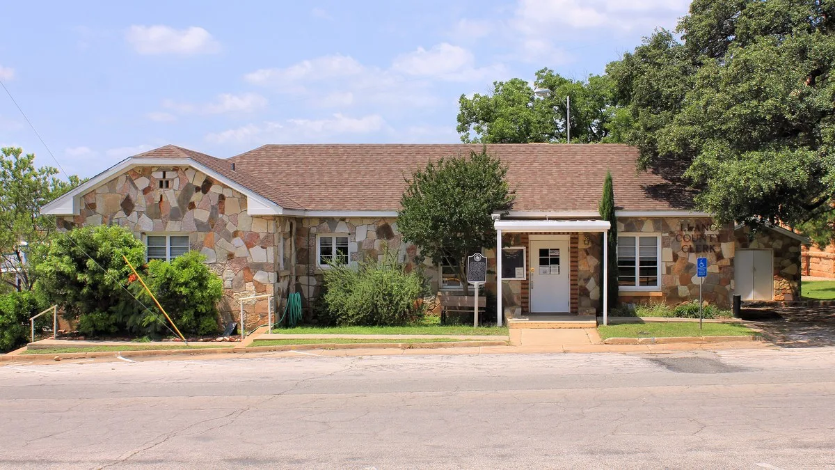 A one-story stone building with a brown shingle roof in Llano that once housed the county library