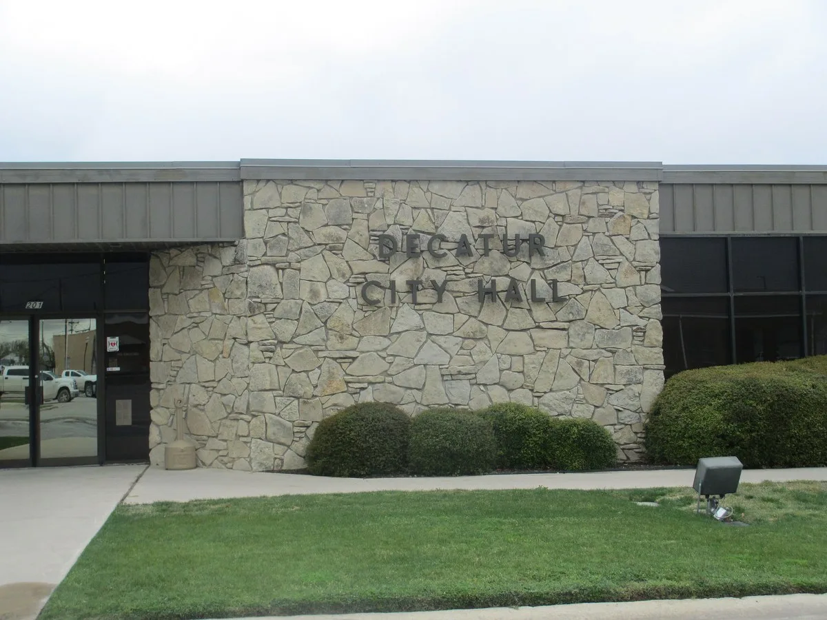 The stone front of Decatur City Hall with its name in metal letters above a row of shrubs