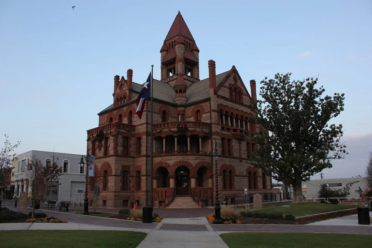 The red granite and sandstone Hopkins County Courthouse in Sulphur Springs with a Texas flag in front