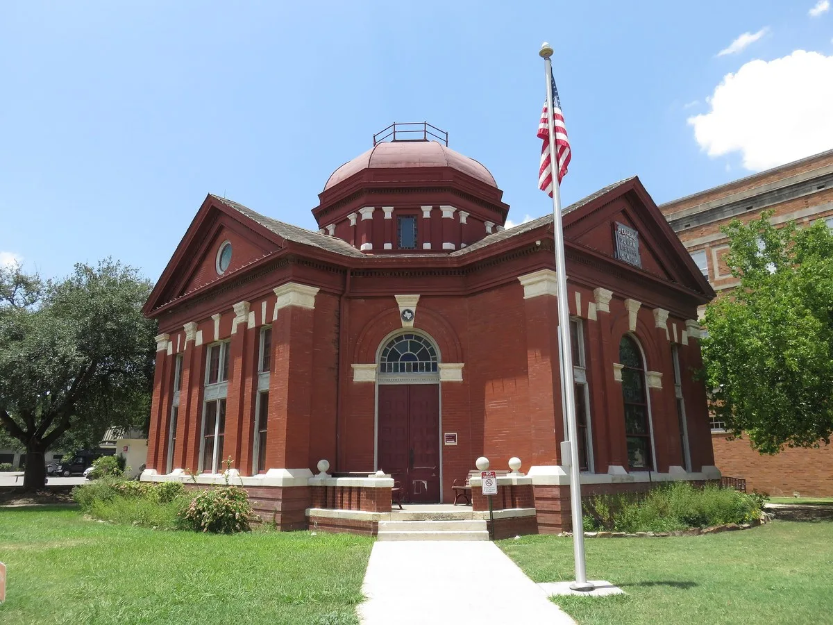 The red brick Dr. Eugene Clark Library in Lockhart, with a domed roof and an American flag out front