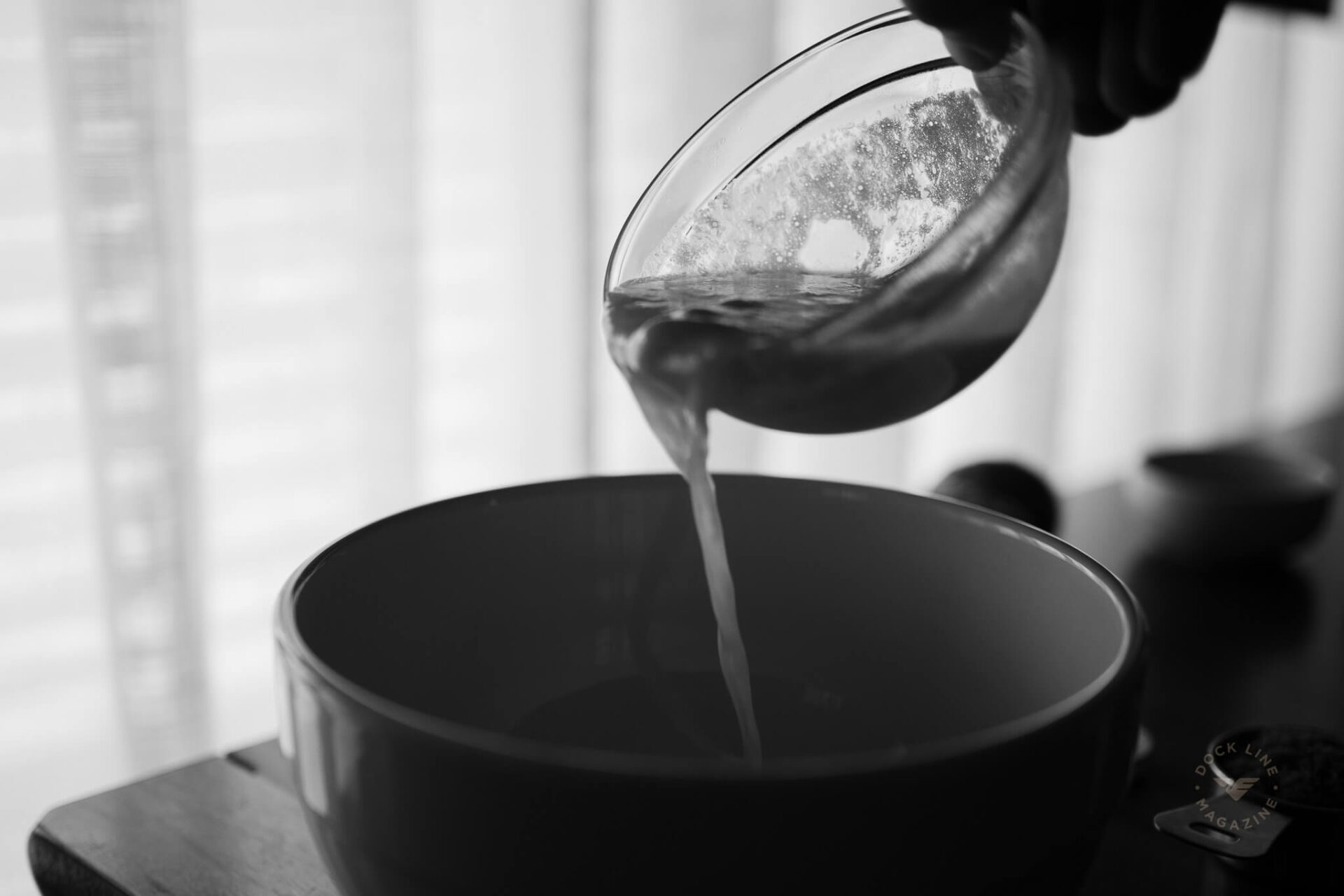 Melted butter being poured from a glass measuring cup into a dark mixing bowl