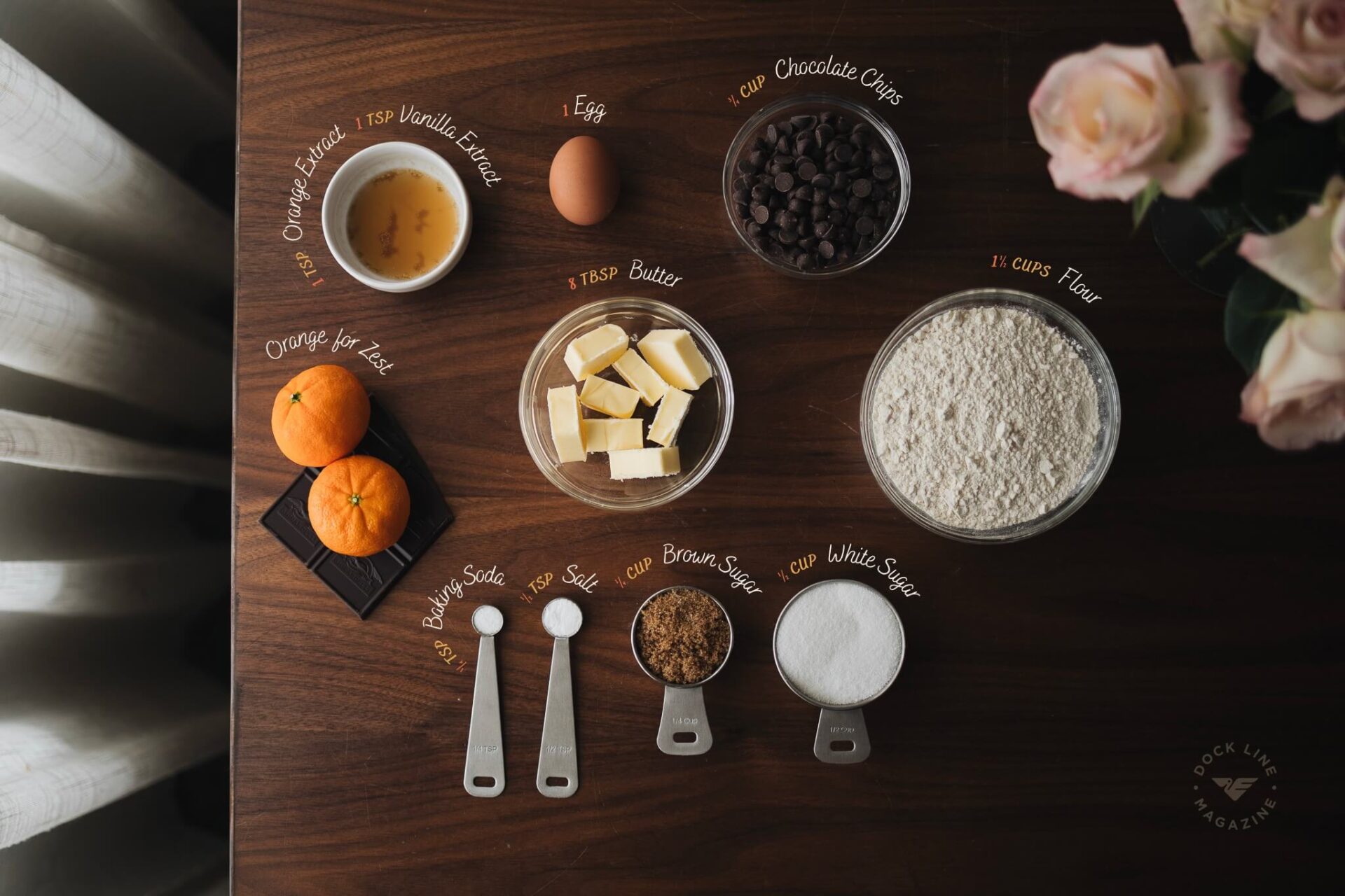 Flat lay of all orange chocolate chip cookie ingredients labeled with measurements on a wooden table
